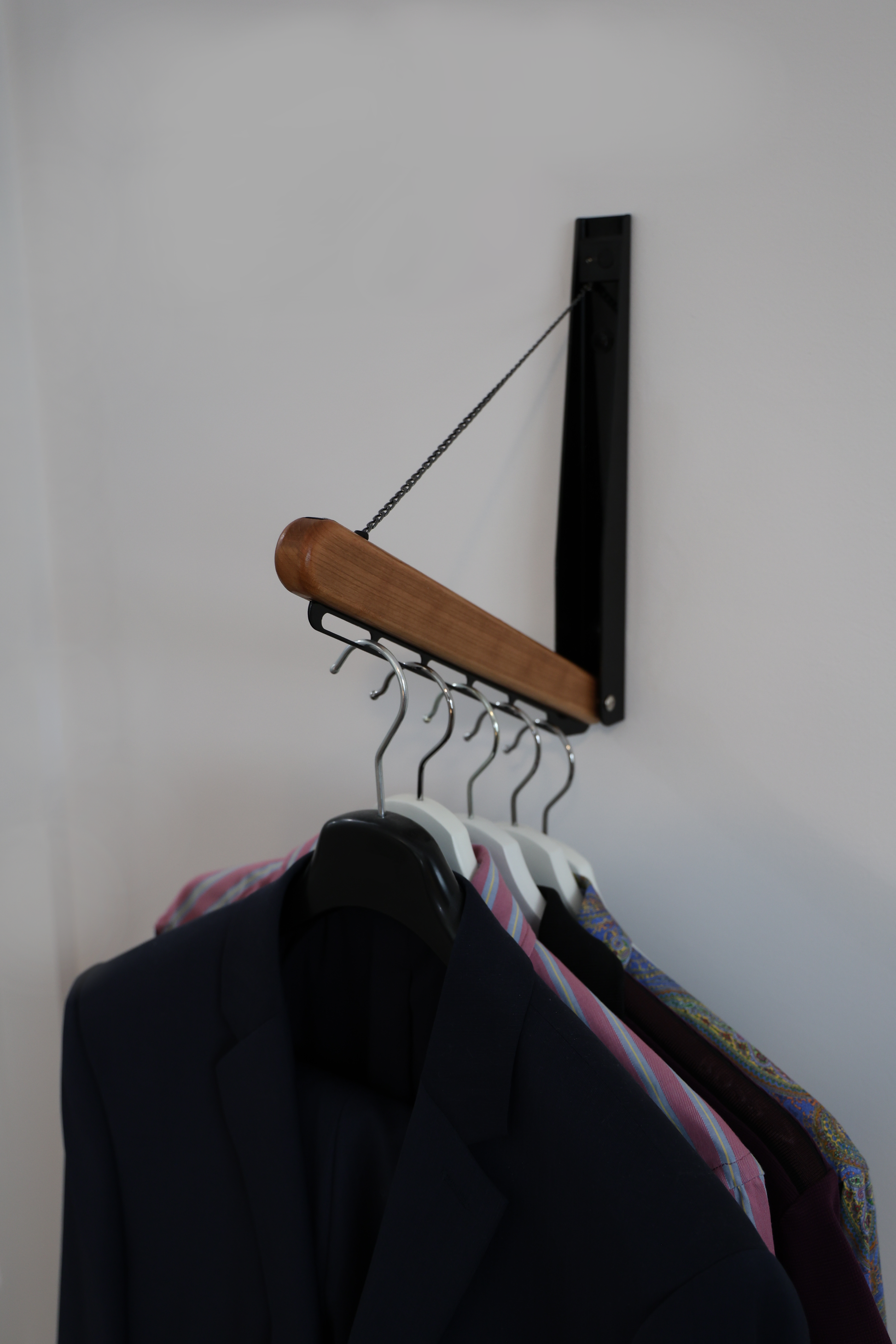 Foldable wall-mounted wooden garment rail with hanging shirts in a minimalist interior.
